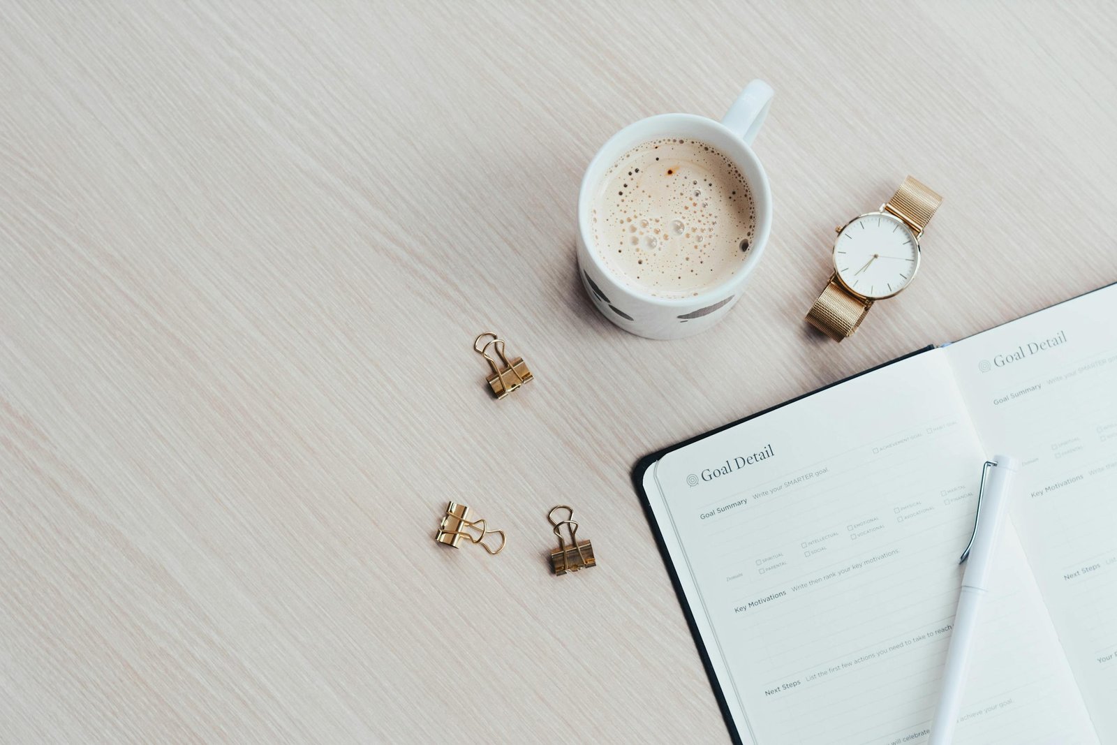 A minimalist desk arrangement featuring a coffee cup, notebook, pen, and wristwatch.