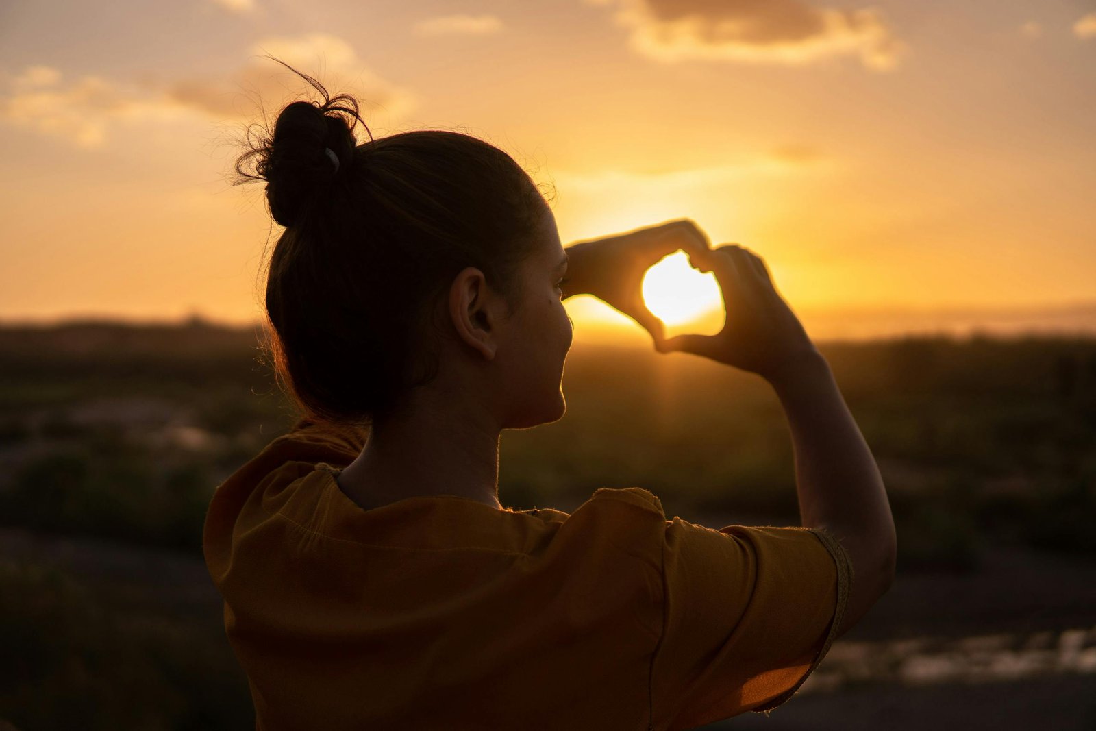 A silhouette of a young woman forming a heart shape at sunset in Kelâat M'Gouna, Morocco.