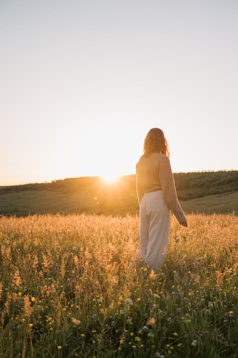 A tranquil moment of a woman in a summer meadow at sunset, capturing natural beauty and serenity.